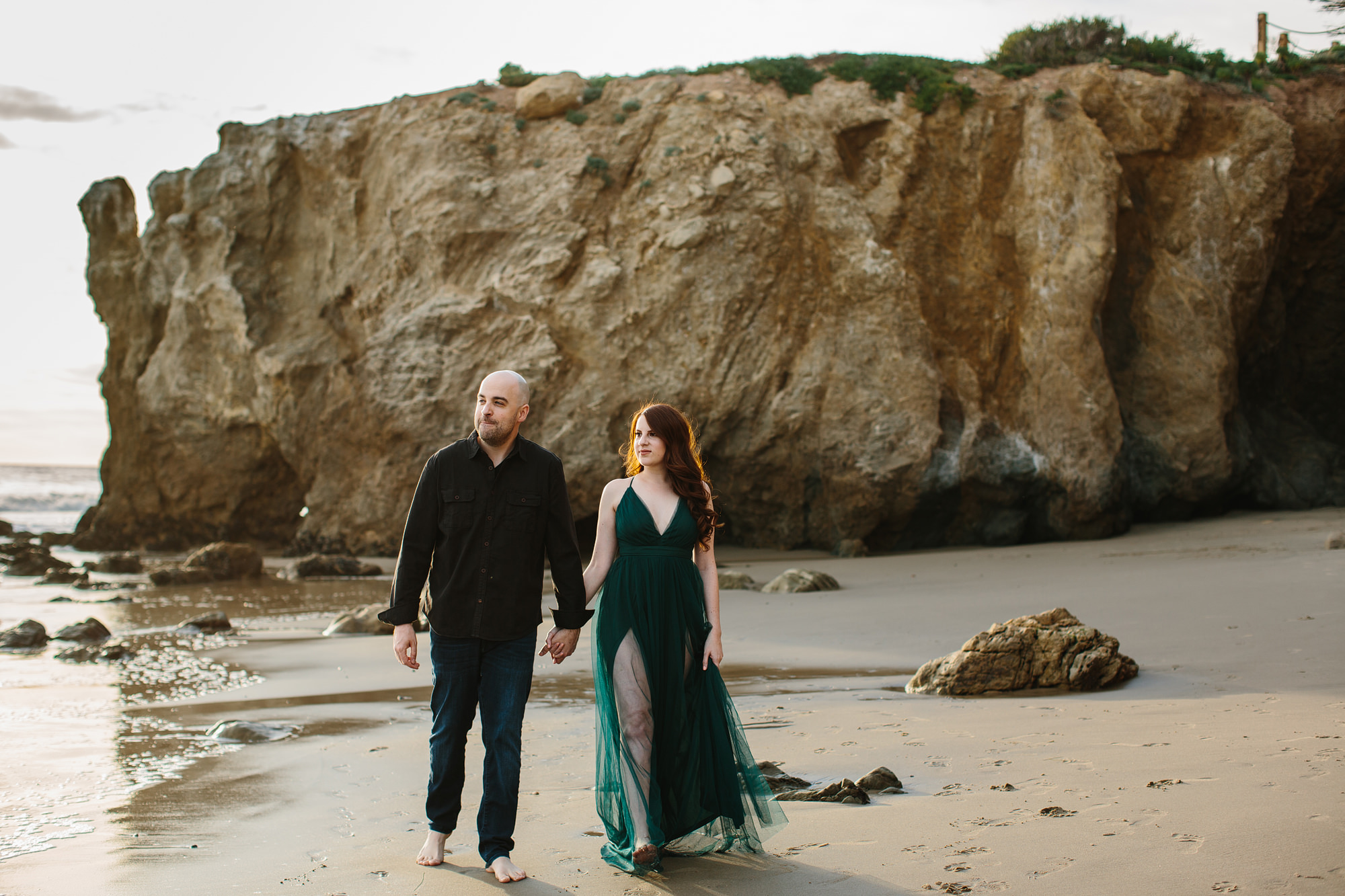malibu california engagement photos of a couple walking along the beach. Bride in green dress,