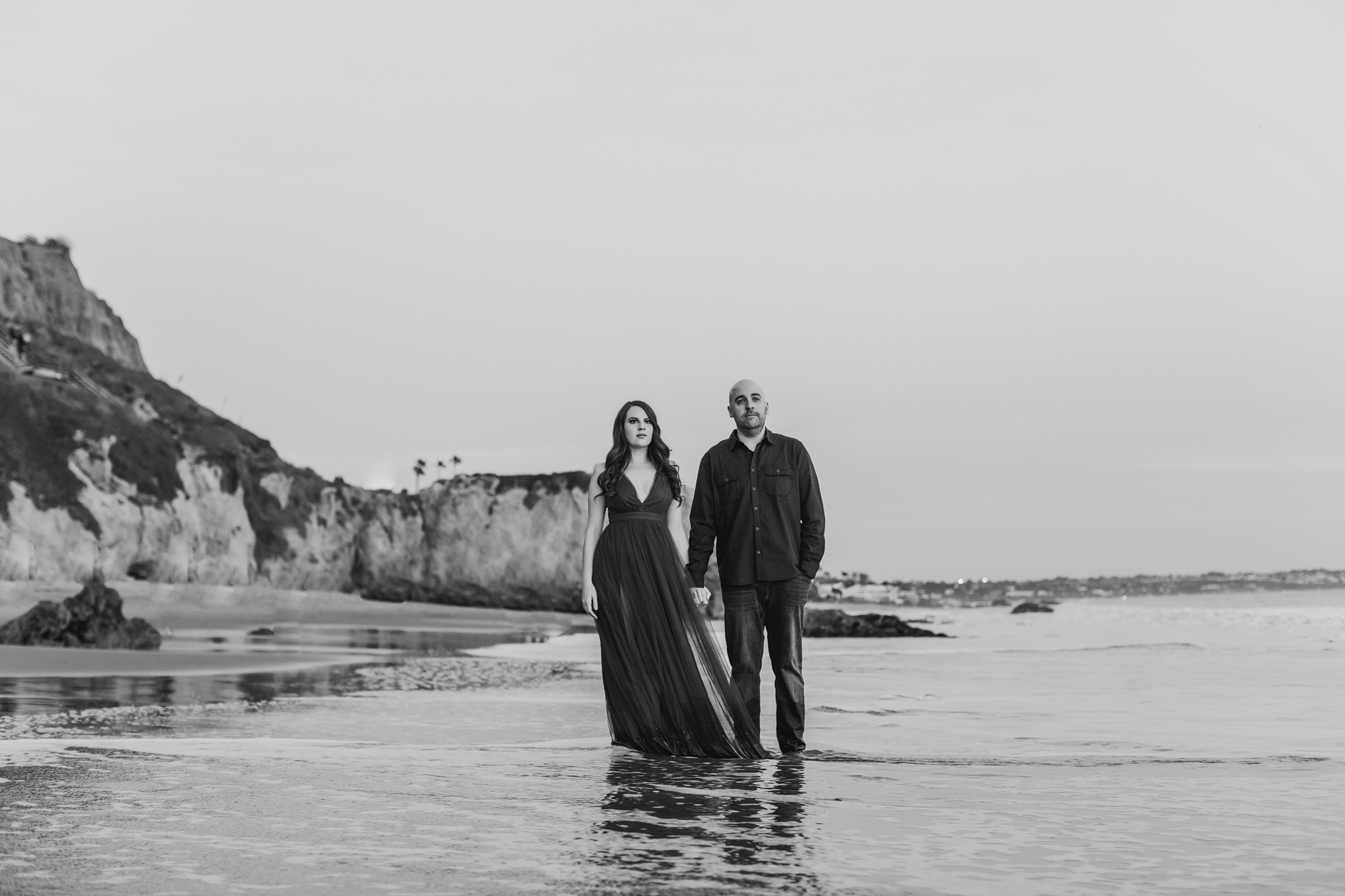 black and white photo of engaged woman and man holding hands in malibu california on the beach
