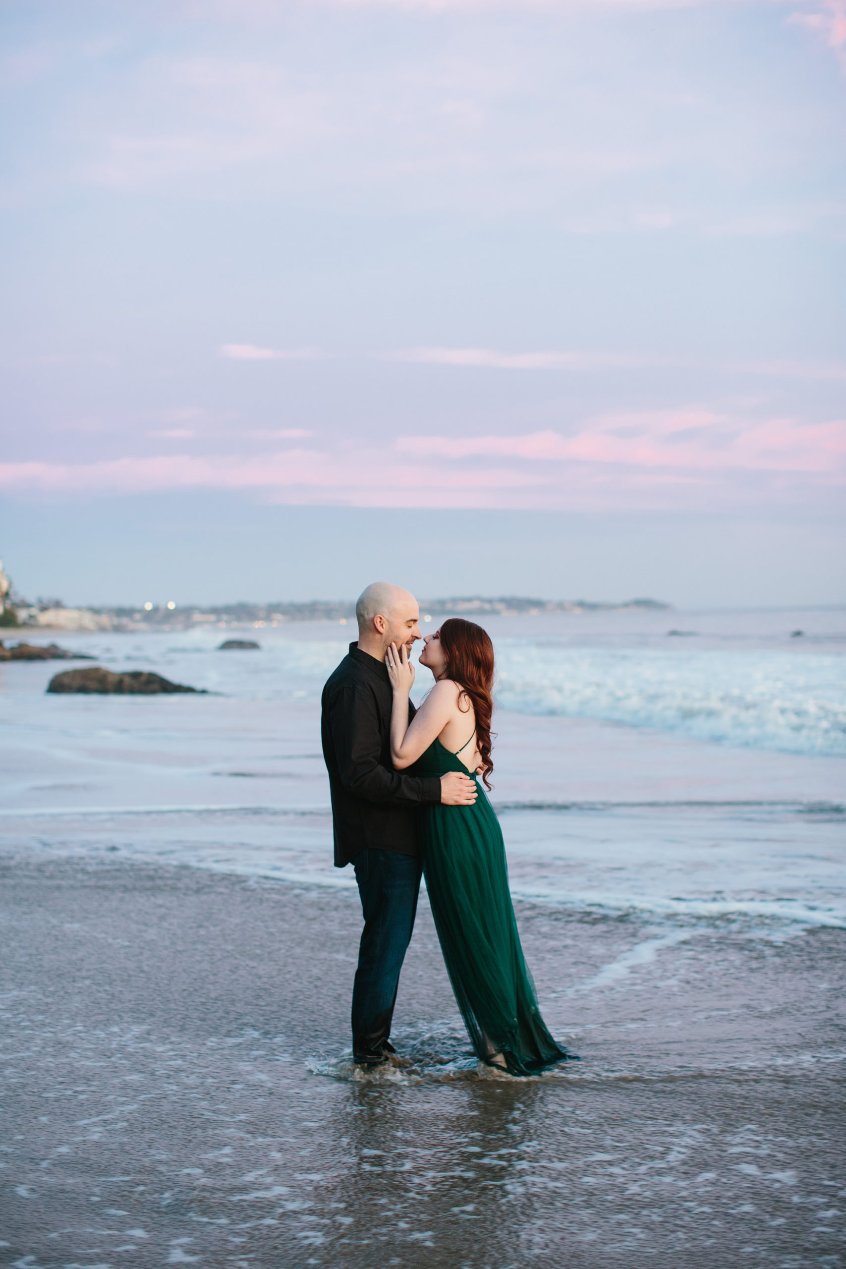 wedding couple standing in the water faces close with the sunset behind them in malibu