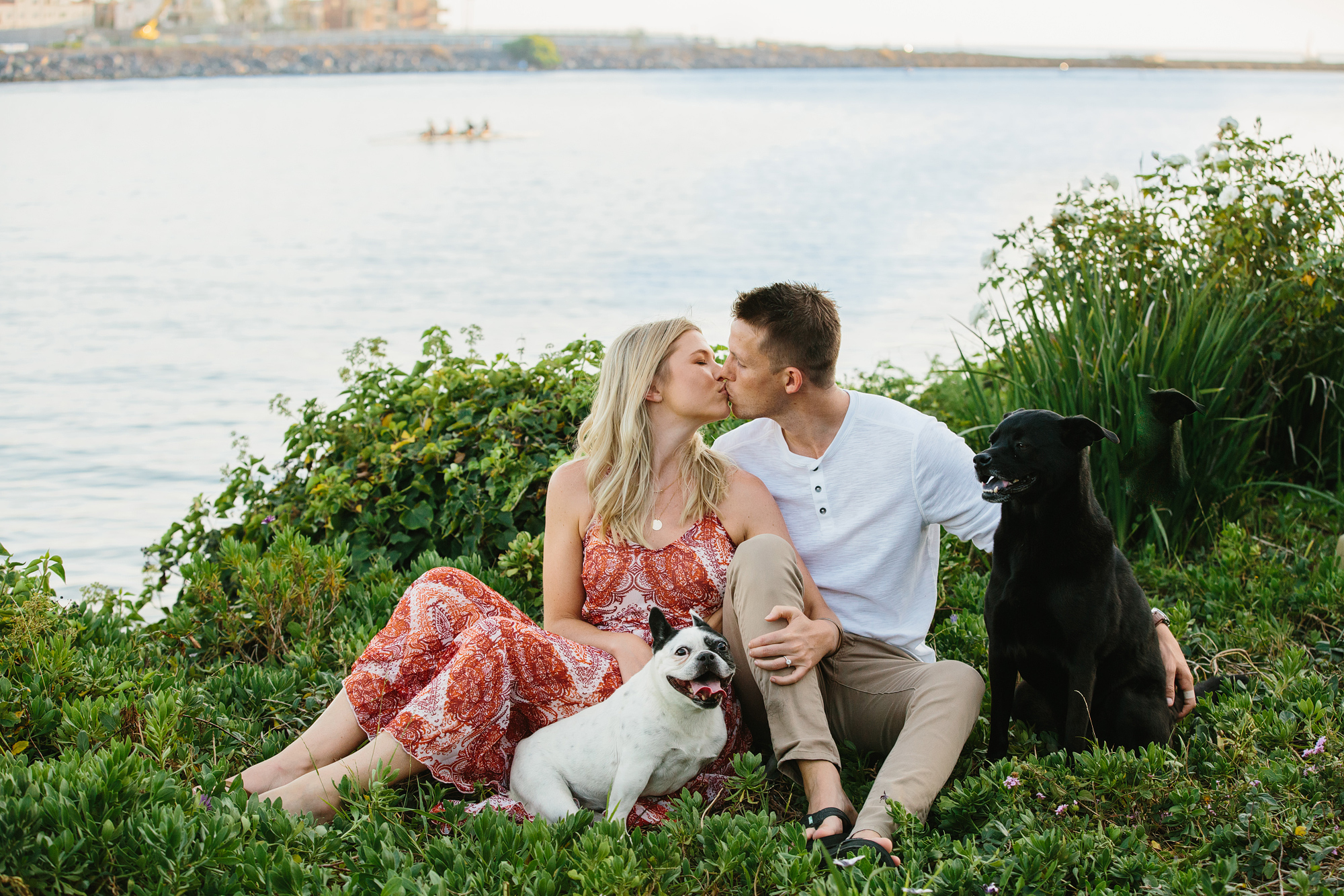 young couple and their two dogs sitting near the water at engagement session