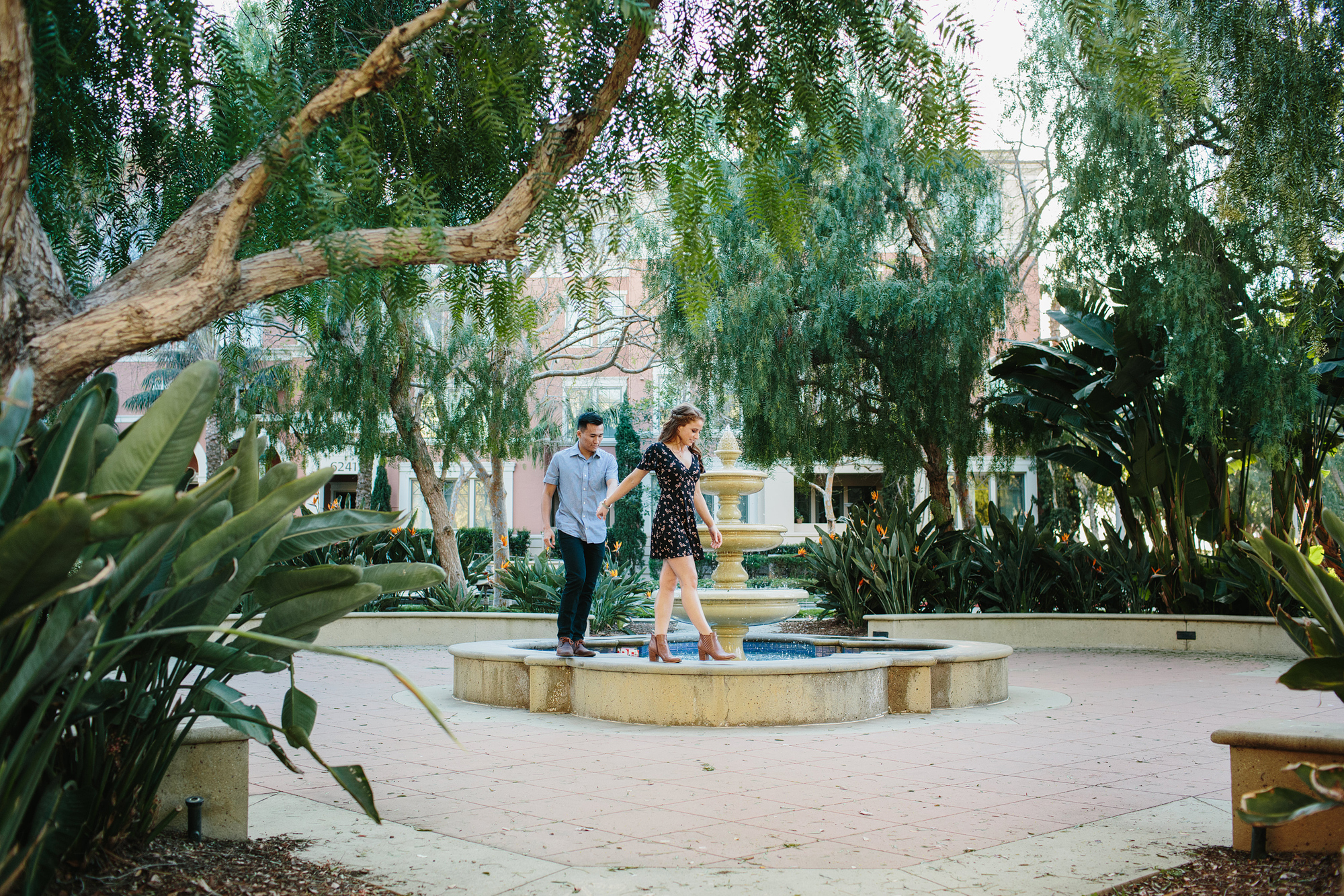 Park engagement photographer. Couple walking on edge of fountain