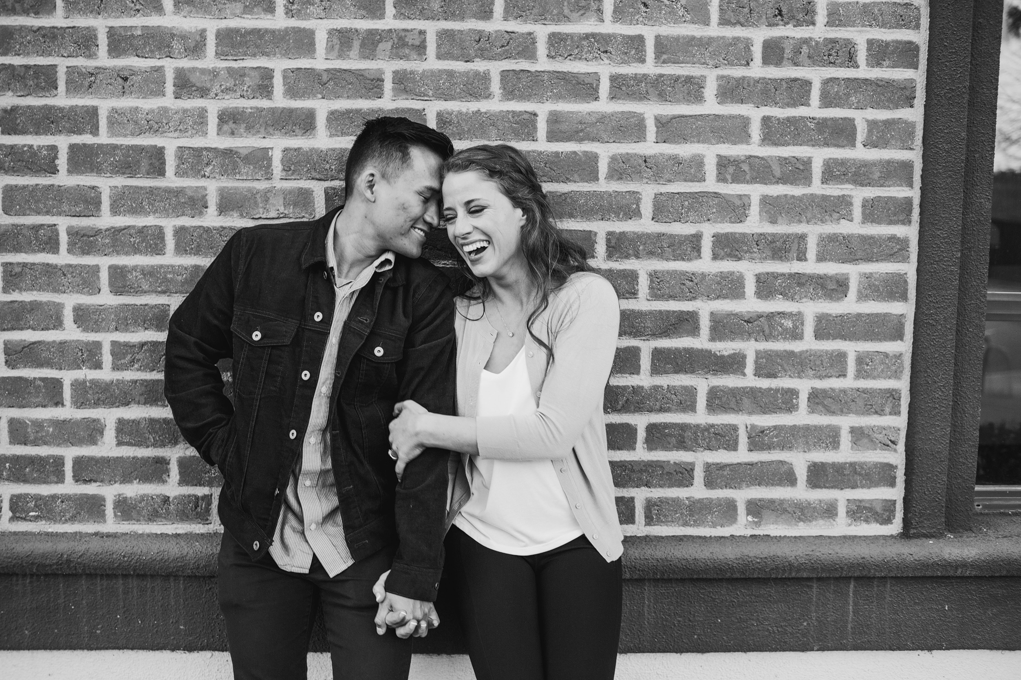 black and white photo of couple laughing against a brick wall
