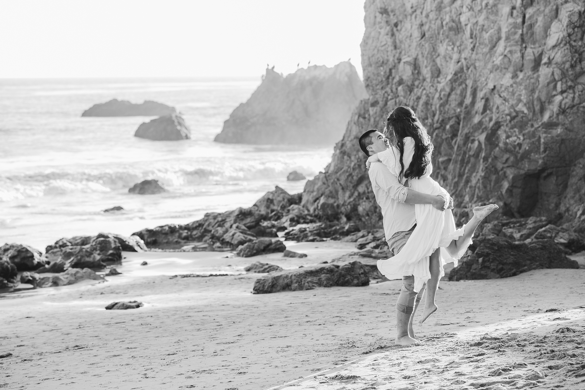black and white photo of groom picking up bride at beach