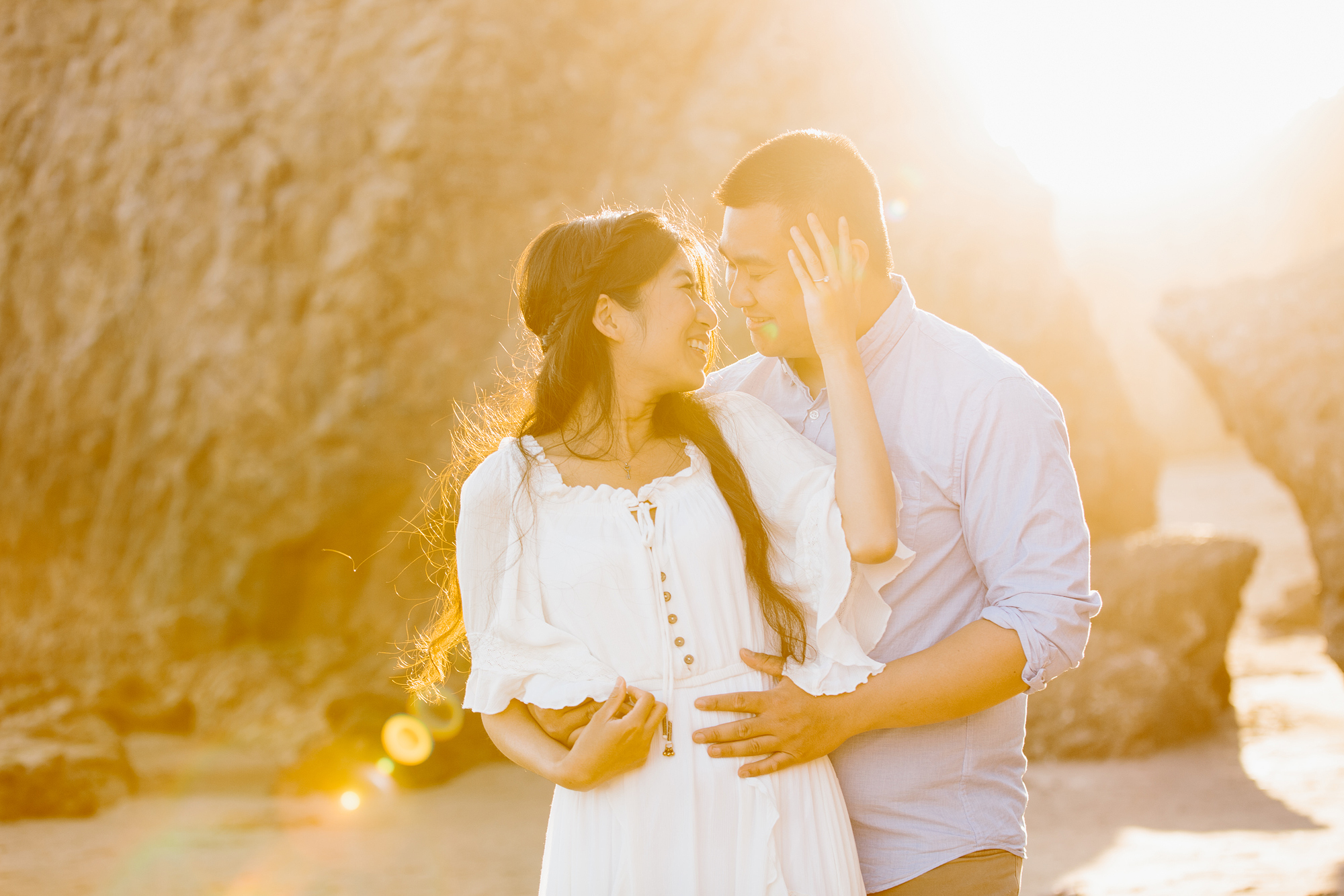 sunkissed engagement photo, groom behind bride to be and she's looking back as the sun shines through